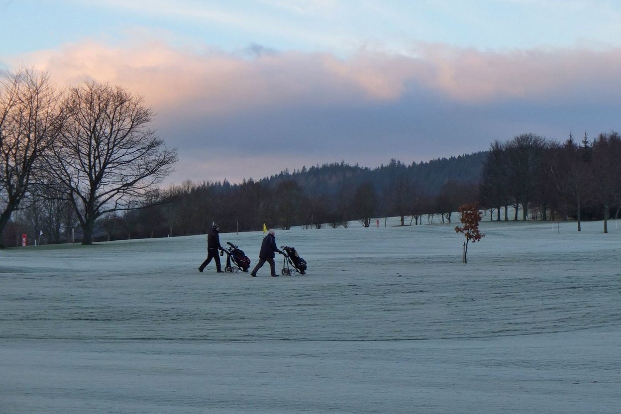 Two golfers pulling carts across a frost-covered golf course on a winter morning