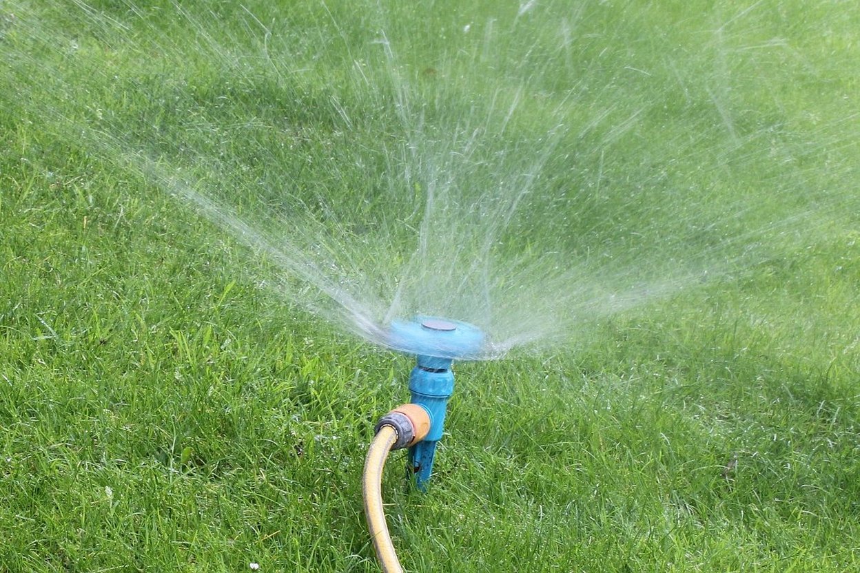 A garden hose with a spray nozzle watering a patch of new lawn