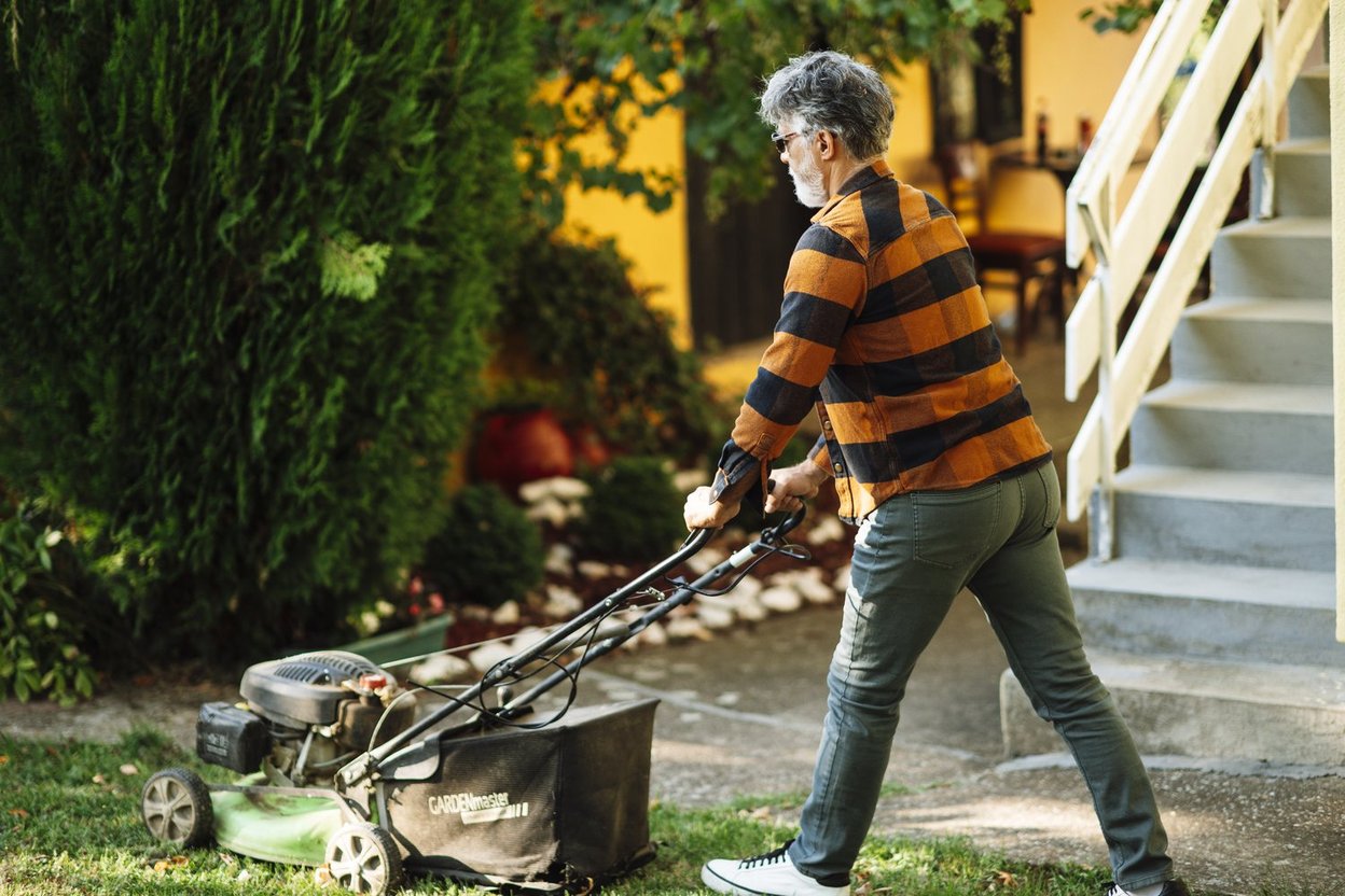 A man pushes a mower across a green suburban lawn